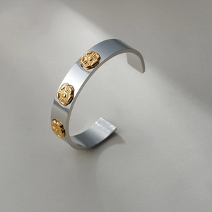 Close-up of stainless steel C-shape cuff bracelet with gold floral relief detail