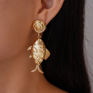 Close-up of golden metallic fish-shaped earrings with textured patterns on model