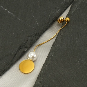 Detail of long gold tassel earring featuring a round white pearl and polished disk pendant