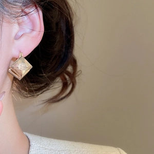 Detail of elegant gold-tone geometric rhombus clip-on earrings worn by a model