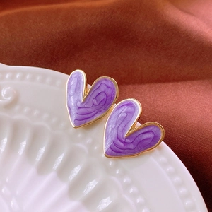 Detail of purple heart earrings with gold trim on white relief ceramic and silk