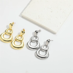 Polished gold and silver double-layered teardrop metal earrings on a minimalist stone