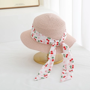 Close-up of pink straw sun hat with cherry pattern ribbon on a golden display stand