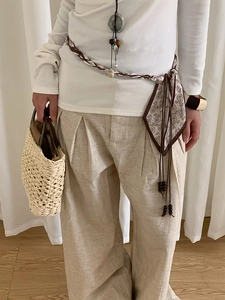 Détail d'une ceinture foulard bohème avec perles en bois sur un pantalon en lin