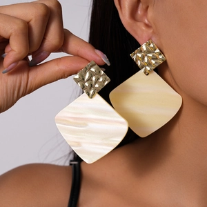 Close-up of geometric acrylic earrings with marble pattern and gold hammered metal detail