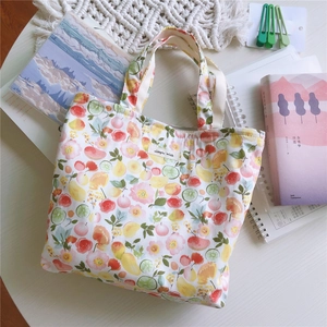 Vue à plat d'un sac cabas en coton fleuri avec imprimés de pêches, citrons et étiquette