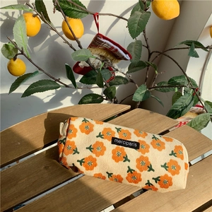 Corduroy pouch with orange floral print on a wooden bench near a lemon tree background