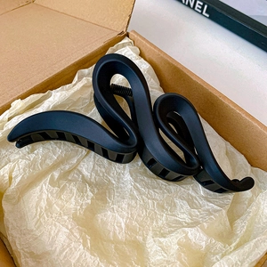 Detail of a matte black S-shaped shark hair claw clip inside a minimalist gift box