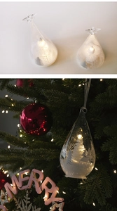Detail of glowing glass Christmas ornaments with snowy trees and warm LED lighting
