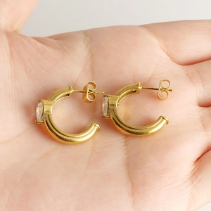 Golden C-shaped stainless steel earrings with zircon stone held in a hand