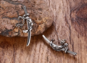 Detail view of silver punk katana sword stud earrings on dark stone and wood background