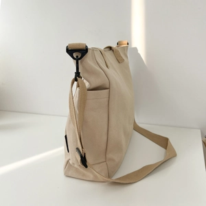 Detail view of beige canvas tote bag with adjustable strap and black metal hardware