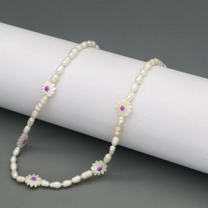 Detail of freshwater pearl necklace featuring purple floral accents on white cylinder stand