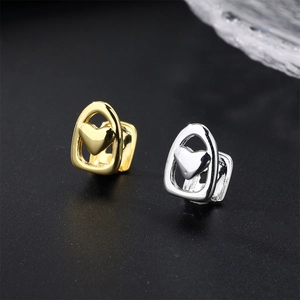 Close-up of gold and silver heart-shaped hollow grillz on a dark textured surface