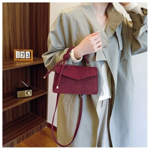 Detail of dark red faux suede handbag featuring unique knotted handles and detachable strap
