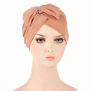 Detail of light brown turban cap featuring a large front bow and rhinestone buckle