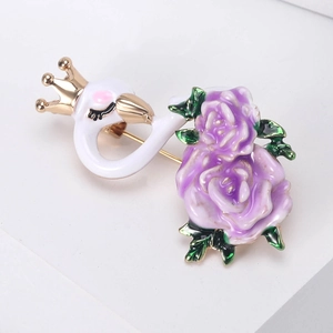 Detail of white swan enamel brooch with golden crown and purple roses on metal surface