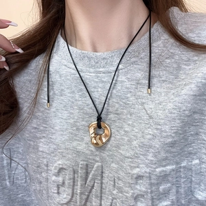 Close-up of gold irregular lava pendant on a black rope chain worn by a model