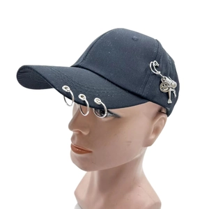 Detail of black baseball cap featuring silver metal rings, safety pin, and smile pendant