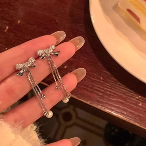 Close-up of silver bow earrings with long tassels, sparkling rhinestones and white pearls