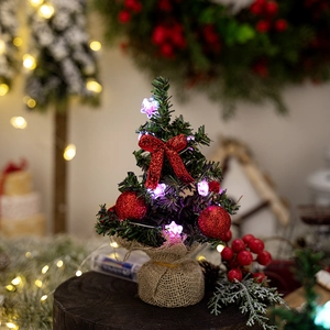 Mini Christmas tree with red bows and LED star light on a rustic burlap base