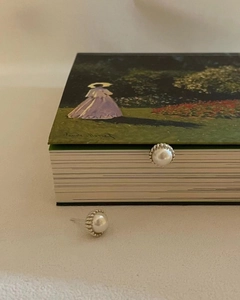 Elegant pearl stud earrings with gear-edged metal base on an artistic Claude Monet book