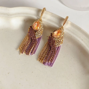 Close-up of golden bohemian fringe earrings with teardrop zircon and purple chains