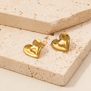Macro shot of minimalist gold heart stud earrings resting on textured stone surfaces