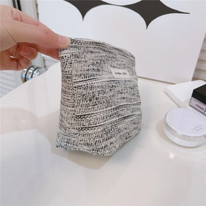 Detail view of woven tweed makeup bag with simple wish label and cosmetic items