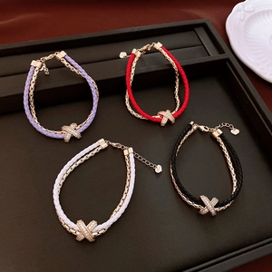 Close-up of double-layer leather and gold-tone chain bracelets with zircon X-charms