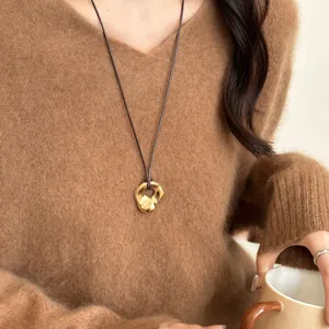 Close-up of irregular gold ring pendant on a brown cord over a cozy mohair sweater