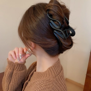 Detail view of a matte black hair claw clip styled on a model in a natural setting