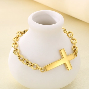 Close-up of golden stainless steel cross bracelet on a white ceramic vase