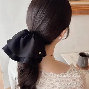 Close-up of a large black satin bow hair claw clip with a subtle gold logo detail