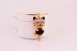 Close-up of a sparkling Maneki Neko keychain with rhinestones on a white ceramic cup