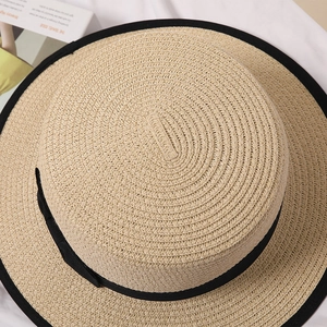 Close-up of a flat top straw sun hat with black ribbon detail on a white fabric surface
