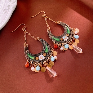 Detailed shot of bohemian crescent moon earrings with green enamel and colorful bead tassels