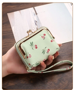 Close-up of light green cherry print card wallet with gold metal clasp and hand strap