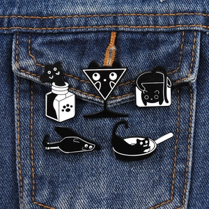 Five cute black and white cat enamel pins styled on a denim jacket pocket edge