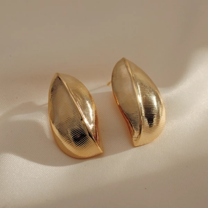 Minimalist gold leaf earrings with brushed metal texture on soft cream satin background