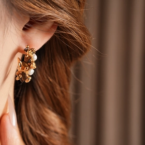 Close-up of C-shaped golden floral earring with tiger eye stone and white pearls on ear