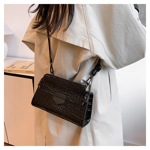Close-up of black crocodile pattern crossbody bag with matte metal buckle on beige trench coat