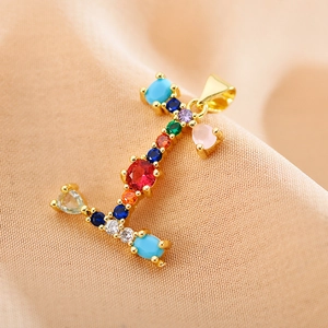 Close-up of golden letter I pendant featuring colorful zircon stones on soft peach fabric