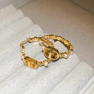 Detail view of gold earrings featuring white pearls and a classic metal logo design