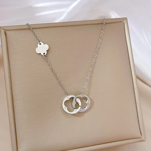 Close-up of silver titanium steel necklace with interlocking clover pendants on beige box