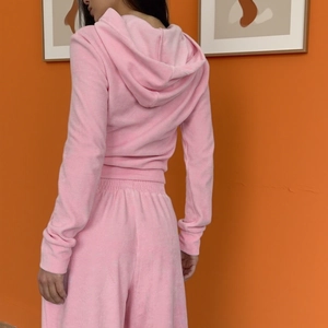 Vista posteriore della tuta in velluto rosa con cappuccio e il drappeggio dei pantaloni dritti