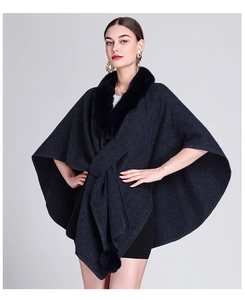 Detailed view of the dark faux fur collar and pom-pom decor on the navy blue knit poncho