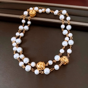 Detail of layered white pearl necklace with intricate hollow gold metal beads