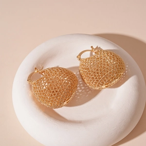 Macro view of gold hollow mesh ball earrings on a white stone tray with soft lighting