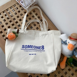 Detailed view of white canvas tote bag with blue lettering and orange fruit pendant